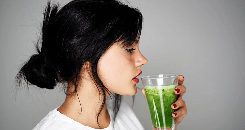 Snygg tjej med svart hår dricker grön juice.
