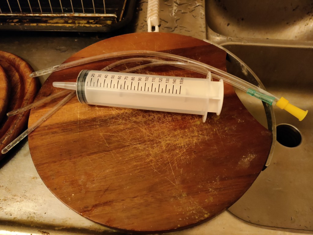 150 ml lavemang spruta på en skärbräda samt tre plastslangar som ska användas för FMT.