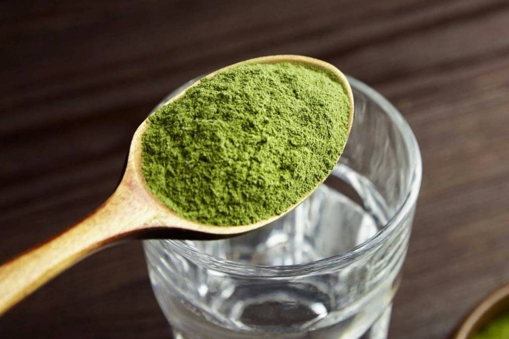 Grönt pulver i en träsked ovanför ett glas vatten.