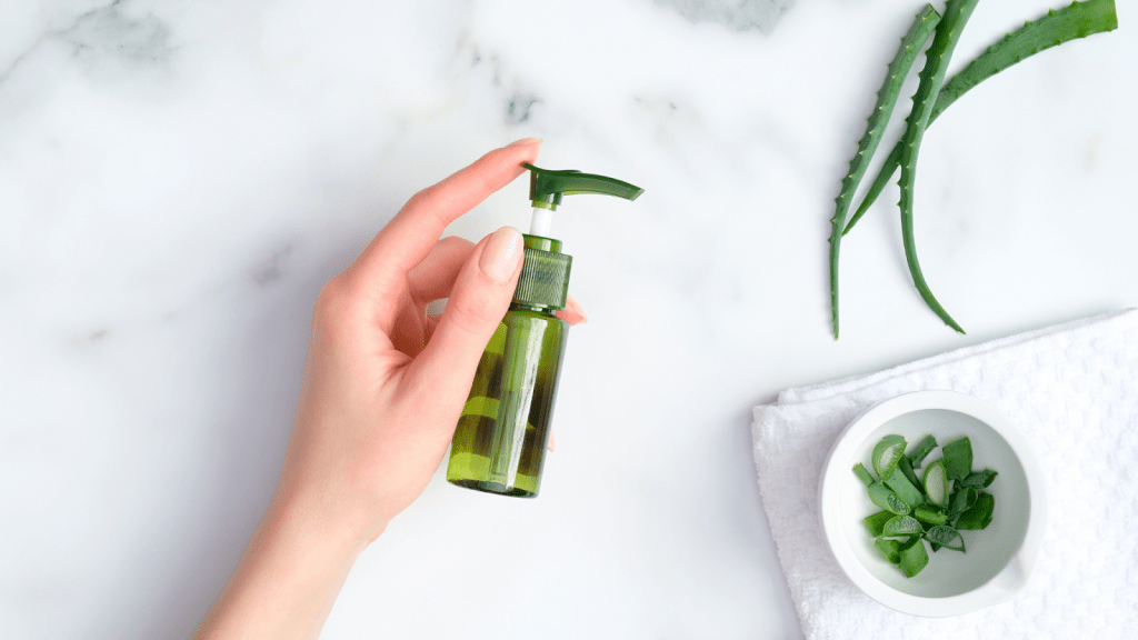 Grön Aloe Vera spray flaska. Aloe Vera löv på ett bord.