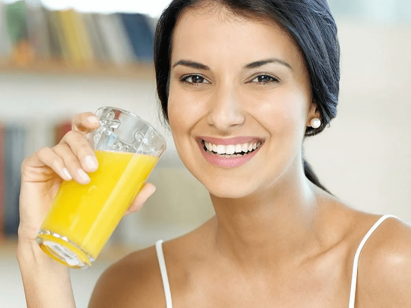 Fin glad skrattande kvinna dricker apelsinjuice ur ett glas.