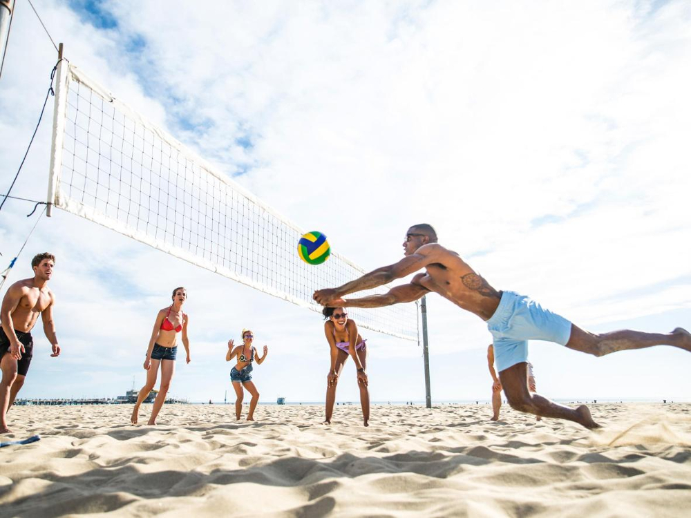 Folk spelar volleyboll på stranden i solen.