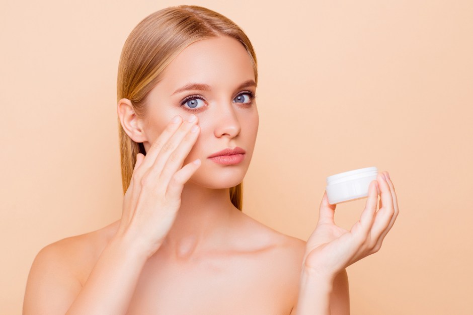 mycket vacker vit kvinna med bar överkropp sätter salva på sitt ansikte med handen orange bakgrund